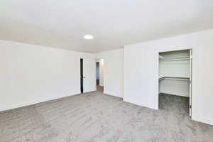 Unfurnished bedroom with light colored carpet and a walk in closet