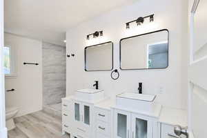 Full bath featuring double vanity, a tile shower, and light wood-type flooring