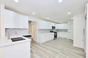 Kitchen with white cabinetry, appliances with stainless steel finishes, light wood-style flooring, recessed lighting, and backsplash