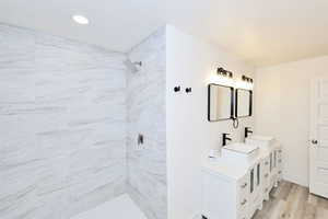 Bathroom featuring double vanity, a tile shower, and light wood-style floors