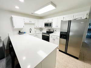 Kitchen with stainless steel appliances, a peninsula, white cabinets, a kitchen breakfast bar, and recessed lighting