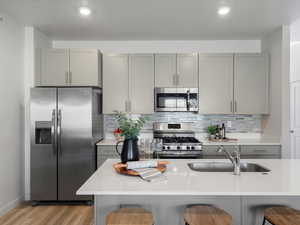 Kitchen featuring gray cabinetry, stainless steel appliances, tasteful backsplash, light stone counters, and a textured ceiling