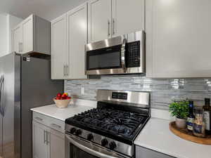 Kitchen with stainless steel appliances, backsplash, and gray cabinets