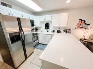 Kitchen featuring appliances with stainless steel finishes, white cabinets, light stone counters, light tile patterned flooring, and recessed lighting