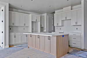 Kitchen featuring light brown cabinetry, white cabinets, a kitchen island, and light stone countertops