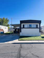 Manufactured / mobile home featuring driveway, an attached carport, a front lawn, and covered porch