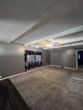 Spare room featuring beam ceiling, ceiling fan, dark carpet, and a textured ceiling