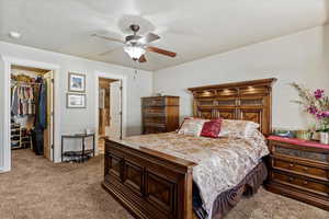 Carpeted bedroom featuring a spacious closet, ensuite bathroom, and ceiling fan