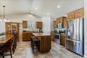 Kitchen featuring appliances with stainless steel finishes, light stone countertops, a kitchen breakfast bar, lofted ceiling, and decorative light fixtures