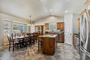 Kitchen featuring vaulted ceiling, stainless steel appliances, decorative light fixtures, light stone counters, and a kitchen island