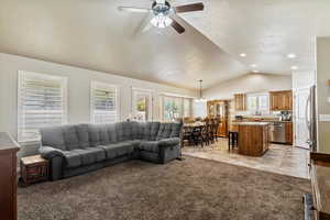 Living area with light carpet, lofted ceiling, light tile patterned floors, a ceiling fan, and a chandelier