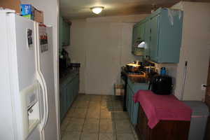 Kitchen featuring white refrigerator with ice dispenser, dark countertops, green cabinets, light tile patterned floors, and a textured ceiling