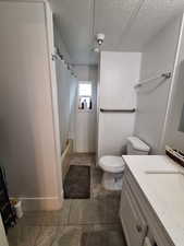 Bathroom featuring vanity, shower / tub combo, a textured ceiling, and dark tile patterned flooring