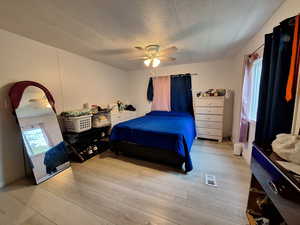 Bedroom featuring multiple windows, light wood-type flooring, ceiling fan, and a textured ceiling