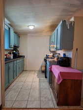Kitchen featuring dark countertops, a textured ceiling, new blue cabinets, stove, and light tile patterned floors
