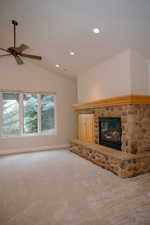Unfurnished living room featuring vaulted ceiling, carpet flooring, ceiling fan, recessed lighting, and a stone fireplace
