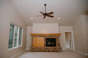 Unfurnished living room with a stone fireplace, carpet floors, vaulted ceiling, ceiling fan, and recessed lighting