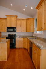Kitchen with light brown cabinetry, black appliances, vaulted ceiling, light wood finished floors, and tile counters