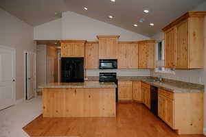 Kitchen featuring light brown cabinets, a center island, black appliances, recessed lighting, and light stone countertops