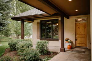 View of exterior entry with a porch, a shingled roof, and stucco siding