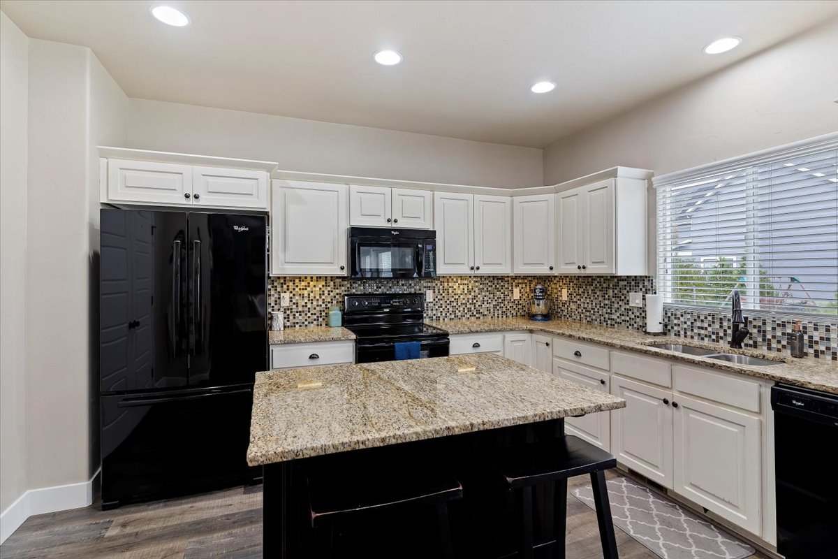 Kitchen with black appliances, white cabinetry, decorative backsplash, light stone counters, and recessed lighting