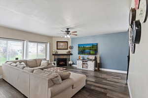 Living area with a tiled fireplace, dark wood-style flooring, and ceiling fan