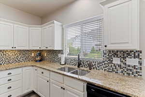 Kitchen featuring white cabinets, light stone countertops, backsplash, and black dishwasher