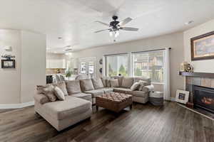 Living area featuring healthy amount of natural light, dark wood finished floors, a tile fireplace, and ceiling fan