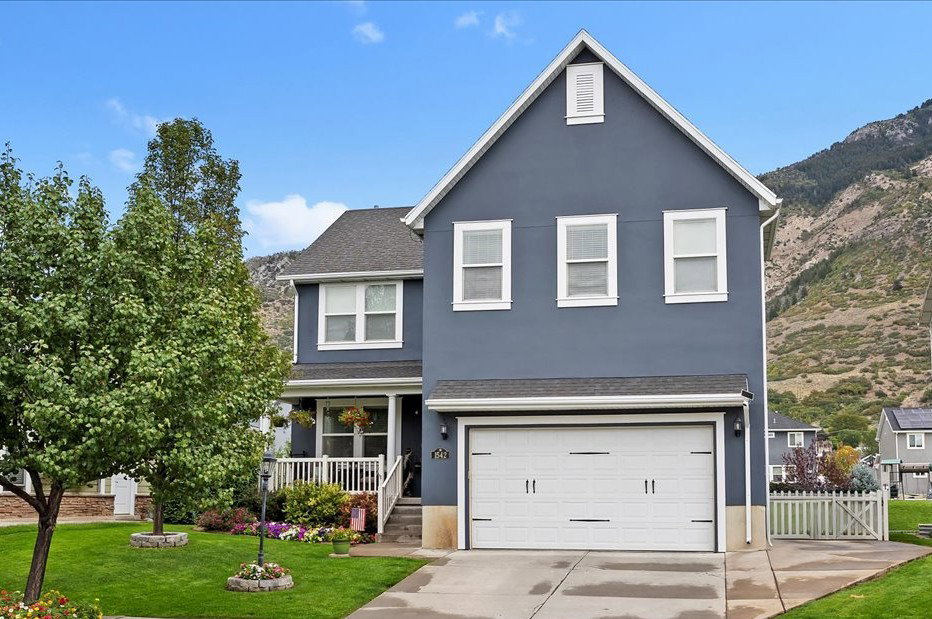 Traditional-style home with covered porch, stucco siding, an attached garage, driveway, and roof with shingles