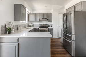 Kitchen with appliances with stainless steel finishes, gray cabinets, a peninsula, light stone counters, and dark wood finished floors