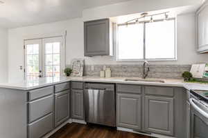 Kitchen with gray cabinets, stainless steel appliances, a peninsula, and light stone countertops