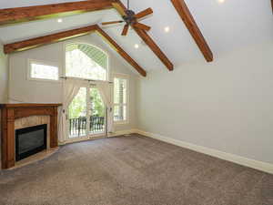 Unfurnished living room with carpet flooring, a premium fireplace, high vaulted ceiling, beamed ceiling, and ceiling fan