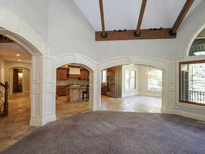Unfurnished living room featuring arched walkways, high vaulted ceiling, stone tile floors, and light carpet