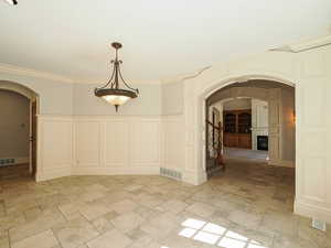 Unfurnished dining area with arched walkways, a decorative wall, a fireplace, stone tile floors, and ornamental molding
