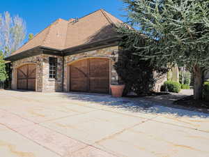 View of front facade featuring stone siding, roof with shingles, driveway, and an attached garage