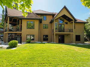 Rear view of property with a balcony, stucco siding, and a yard