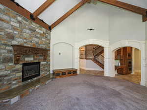 Unfurnished living room with high vaulted ceiling, arched walkways, beamed ceiling, a stone fireplace, and carpet floors