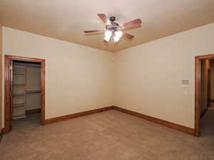 Unfurnished bedroom with a walk in closet, carpet flooring, and a ceiling fan