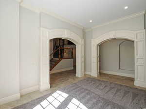 Unfurnished bedroom featuring arched walkways, ornamental molding, light stone finish floors, and recessed lighting