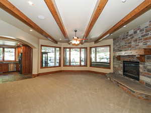 Unfurnished living room with beamed ceiling, a fireplace, light carpet, recessed lighting, and arched walkways