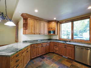 Kitchen featuring open shelves, brown cabinets, appliances with stainless steel finishes, hanging light fixtures, and dark stone finish floors