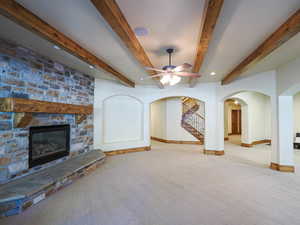 Unfurnished living room featuring a stone fireplace, arched walkways, carpet, beam ceiling, and stairs