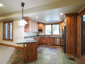 Kitchen featuring brown cabinetry, recessed lighting, dishwasher, freestanding refrigerator, and pendant lighting