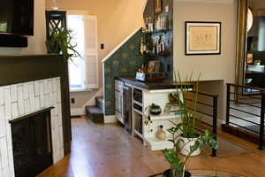 Bar with stairway, open shelves, light wood-type flooring, dark countertops, and a fireplace
