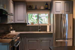 Kitchen with appliances with stainless steel finishes, decorative backsplash, dark countertops, and gray cabinetry