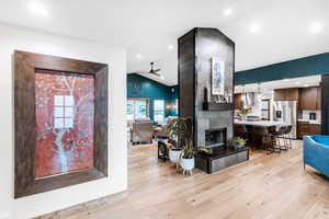 Living room with lofted ceiling, light wood-type flooring, a tiled fireplace, a ceiling fan, and recessed lighting