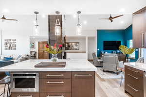 Kitchen with a ceiling fan, open floor plan, light wood-style flooring, a breakfast bar, and decorative light fixtures