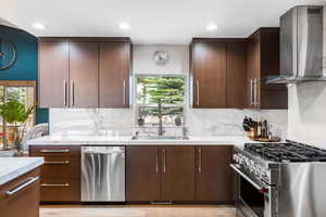 Kitchen featuring appliances with stainless steel finishes, wall chimney range hood, recessed lighting, decorative backsplash, and light wood-style floors