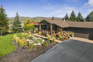 View of front of property with stone siding, asphalt driveway, a garage, a deck with mountain view, and a front lawn