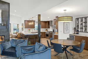 Dining space featuring beverage cooler, lofted ceiling, light wood-style flooring, recessed lighting, and a tiled fireplace